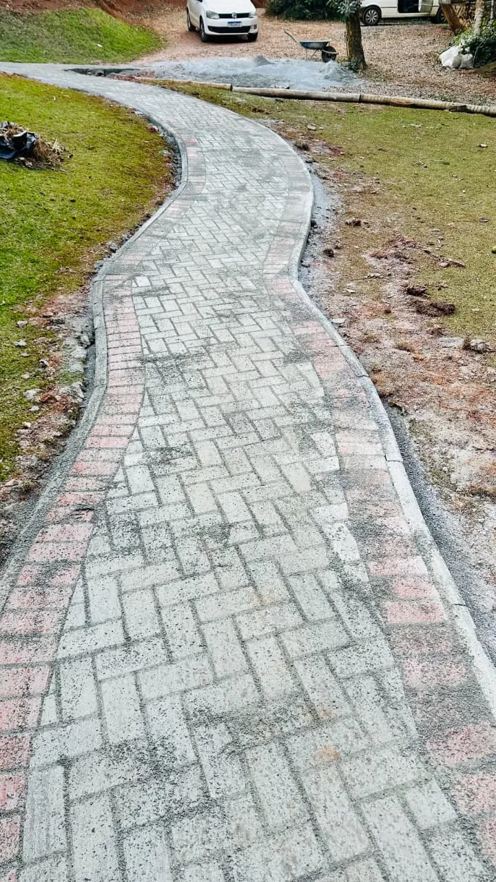 Caminho sinuoso em piso intertravado com bordas, atravessando um gramado